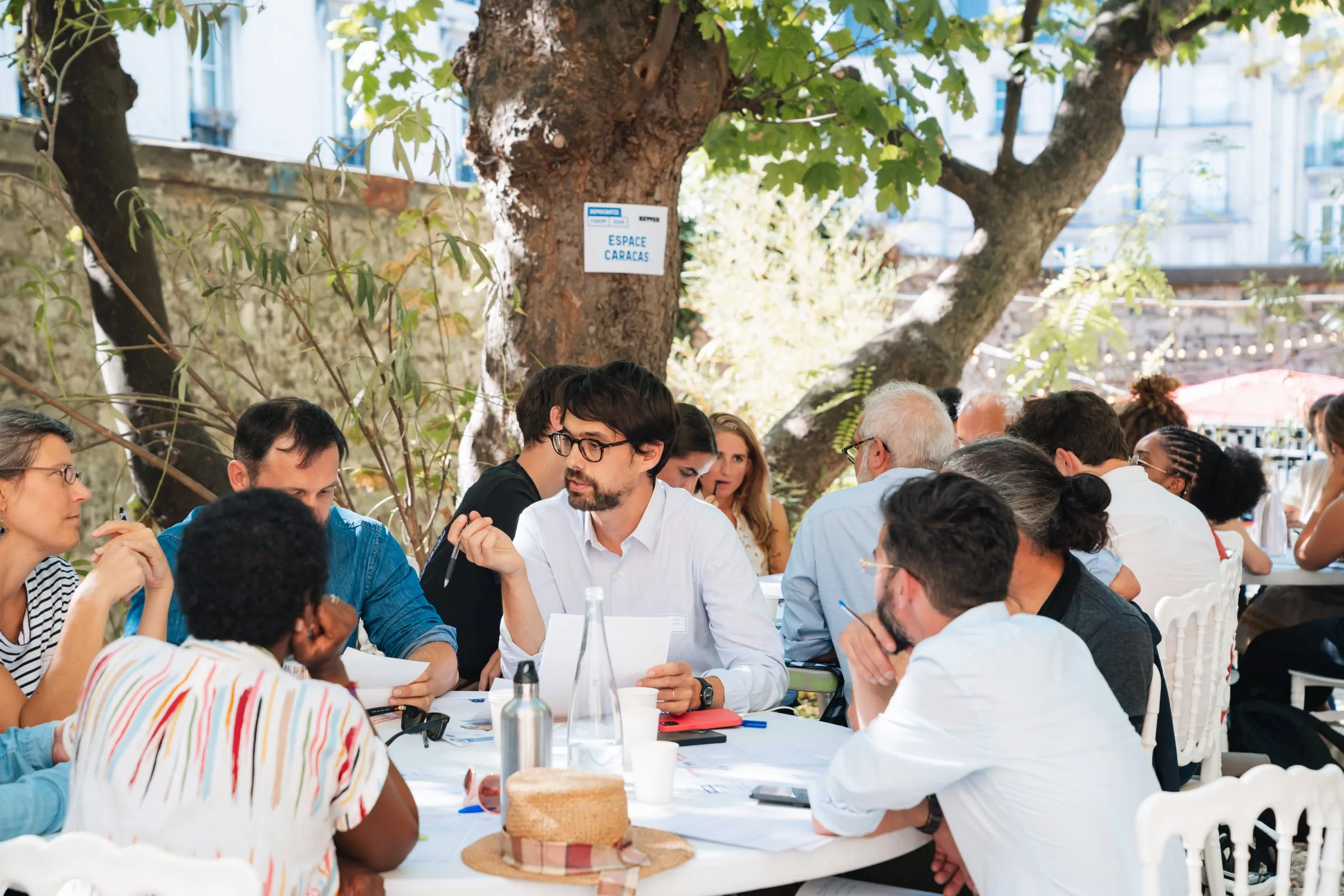 Participants réunis autour d'une table sous les arbres, sous le panneau « Espace Caracas ».